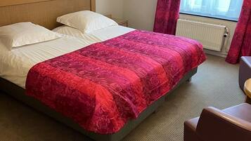 Une chambre d’hôtel avec un lit, une chaise, un radiateur et une fenêtre avec des rideaux.