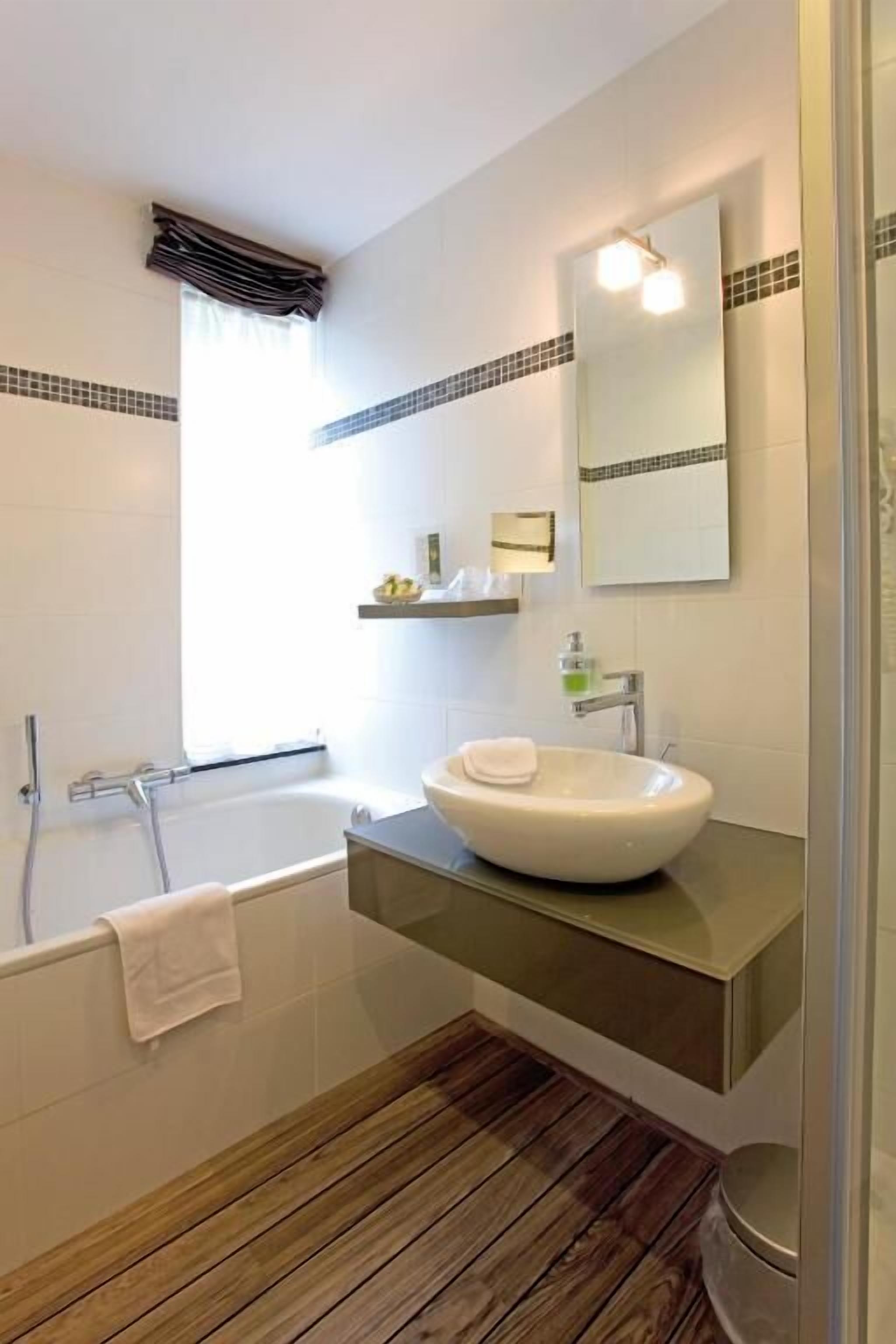 A modern bathroom with a freestanding bathtub, a large mirror, and a wooden floor.