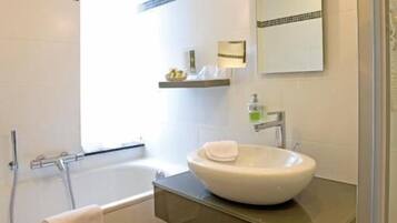 A modern bathroom with a freestanding bathtub, a large mirror, and a wooden floor.