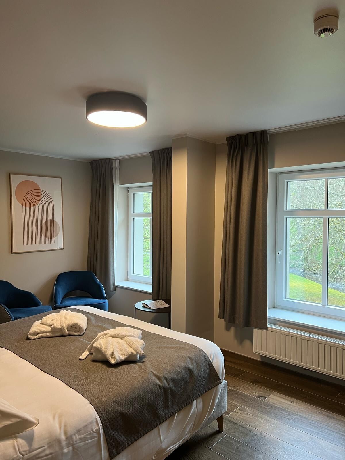 A hotel room with a large bed, two chairs, a small table, and a window with curtains.