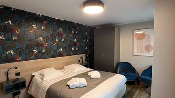 Een moderne hotelkamer met een groot bed, een hoofdeinde met een ingebouwde lamp, een nachtkastje, een kledingkast en twee blauwe stoelen.