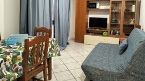 A living room with a sofa, a television, a wooden cabinet, and a dining table with a cactus tablecloth. - Essences of Sicily Apartment (Letojanni)