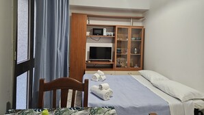 A bedroom with a bed, a wooden wardrobe, a television, and a table with a patterned tablecloth. - Essences of Sicily Apartment (Letojanni)