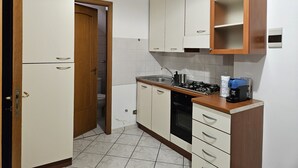 A compact kitchen with white cabinets, a stove, and a coffee maker. - Essences of Sicily Apartment (Letojanni)