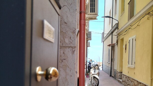A narrow street with a building entrance, a parked scooter, and a clear sky. - Essences of Sicily Apartment (Letojanni)