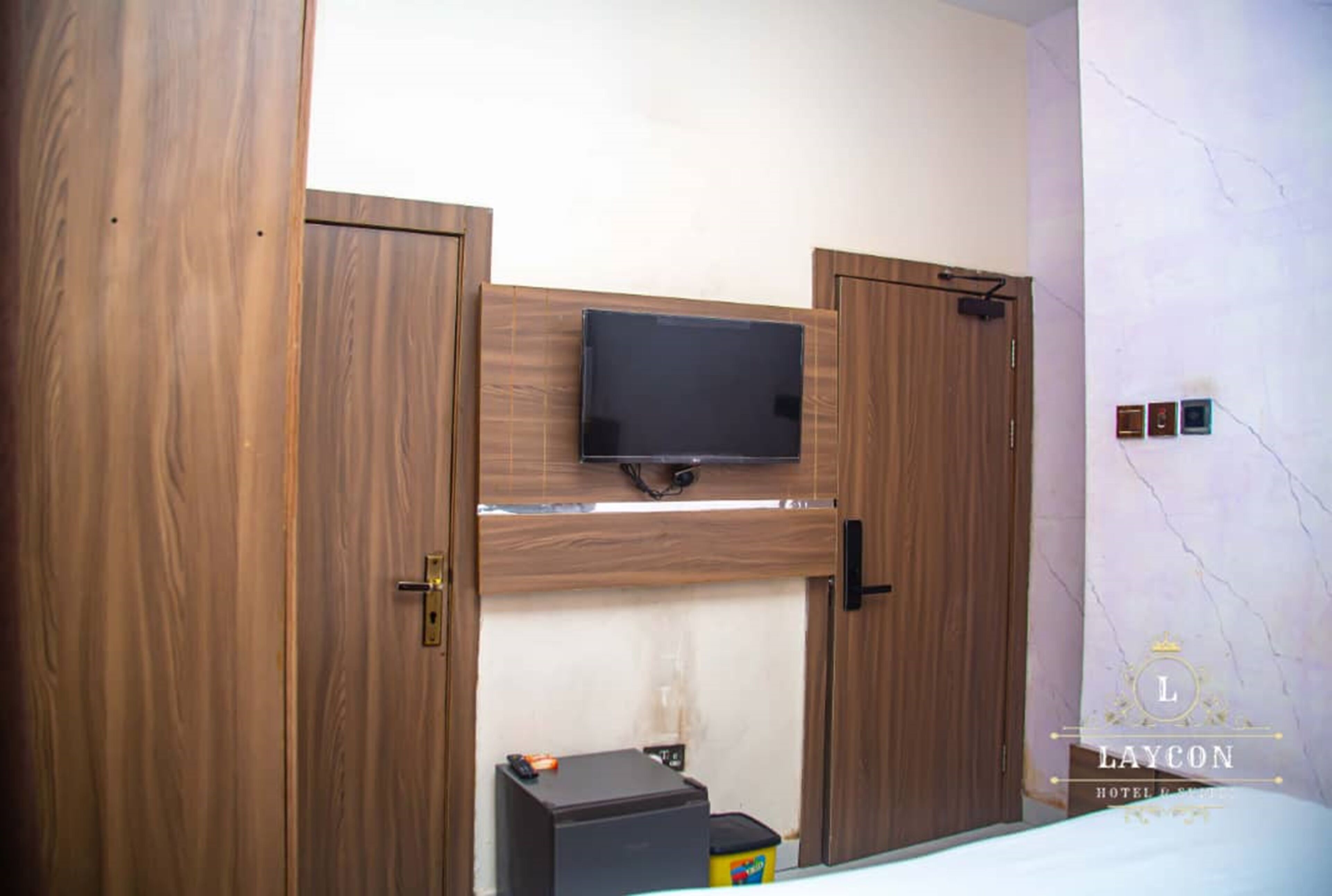 A bedroom with a bed, a television mounted on a wooden cabinet, and a small desk with a chair.