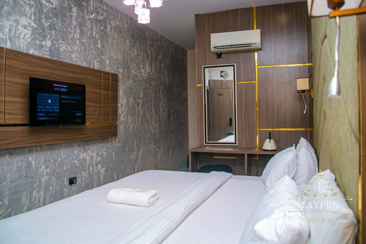 Ett modernt hotellrum med en stor säng, en väggmonterad tv, en spegel och en väggpanel i trä.