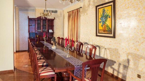 Una sala da pranzo con un lungo tavolo in legno, sedie, un lampadario e un mobiletto.