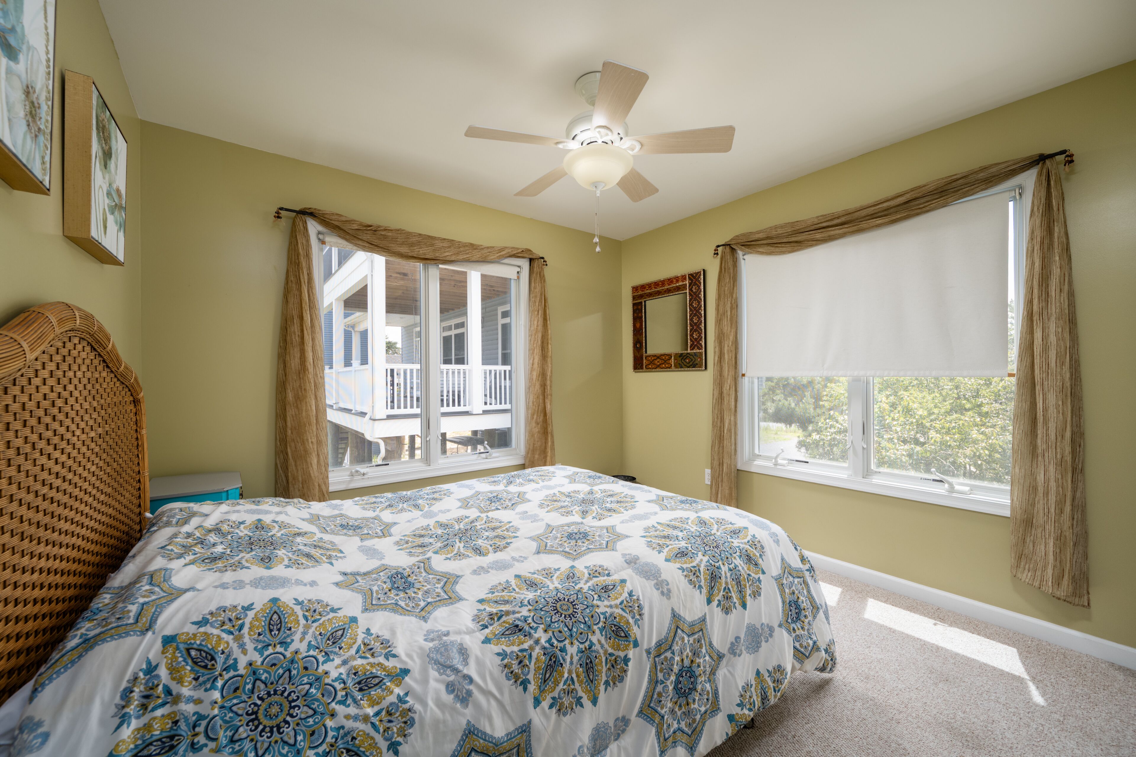 A bedroom with a bed, a ceiling fan, a window with curtains, and a balcony visible through the window.
