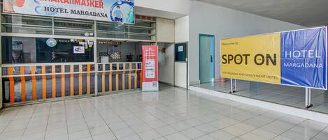 A hotel lobby with a reception desk, a sign for 'Area Wajib Vakkin & Pakai Masker', and a 'Spot On Hotel Margadana' sign.