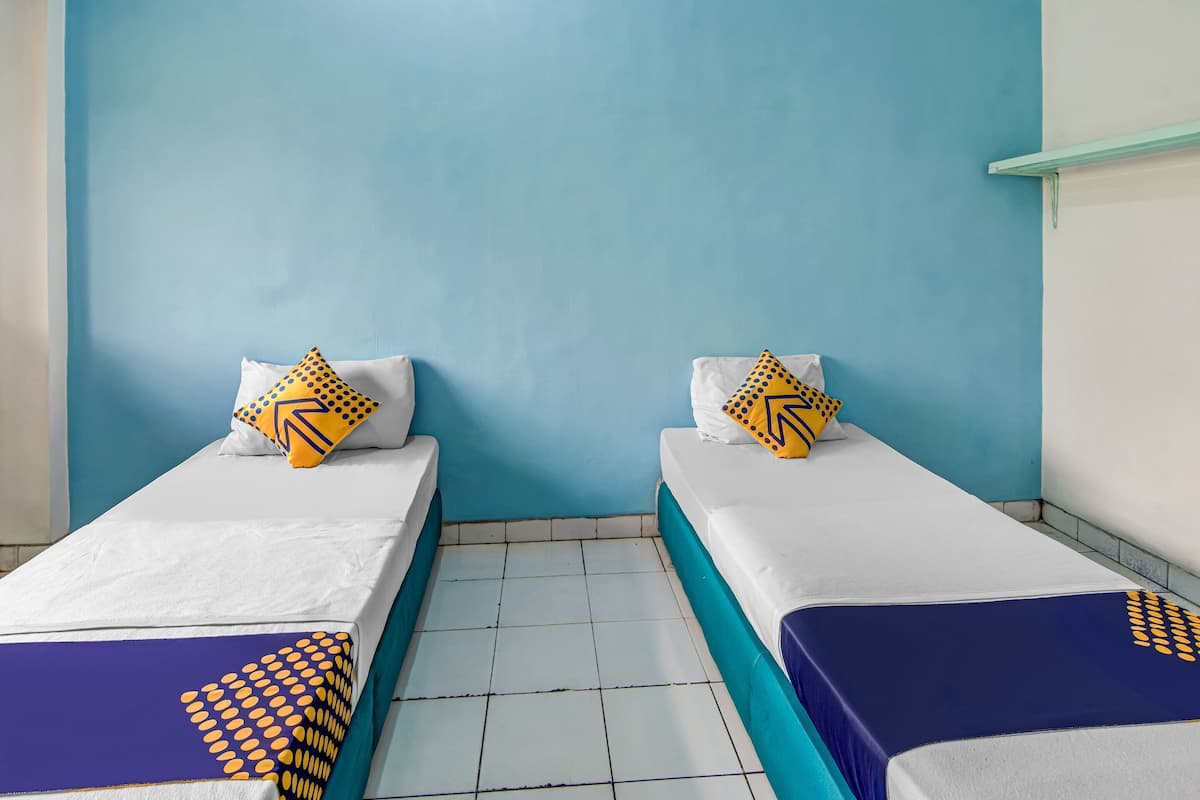 Une chambre avec deux lits simples, chacun doté d’un matelas blanc et de draps bleus, ainsi que d’oreillers assortis à motifs jaunes.