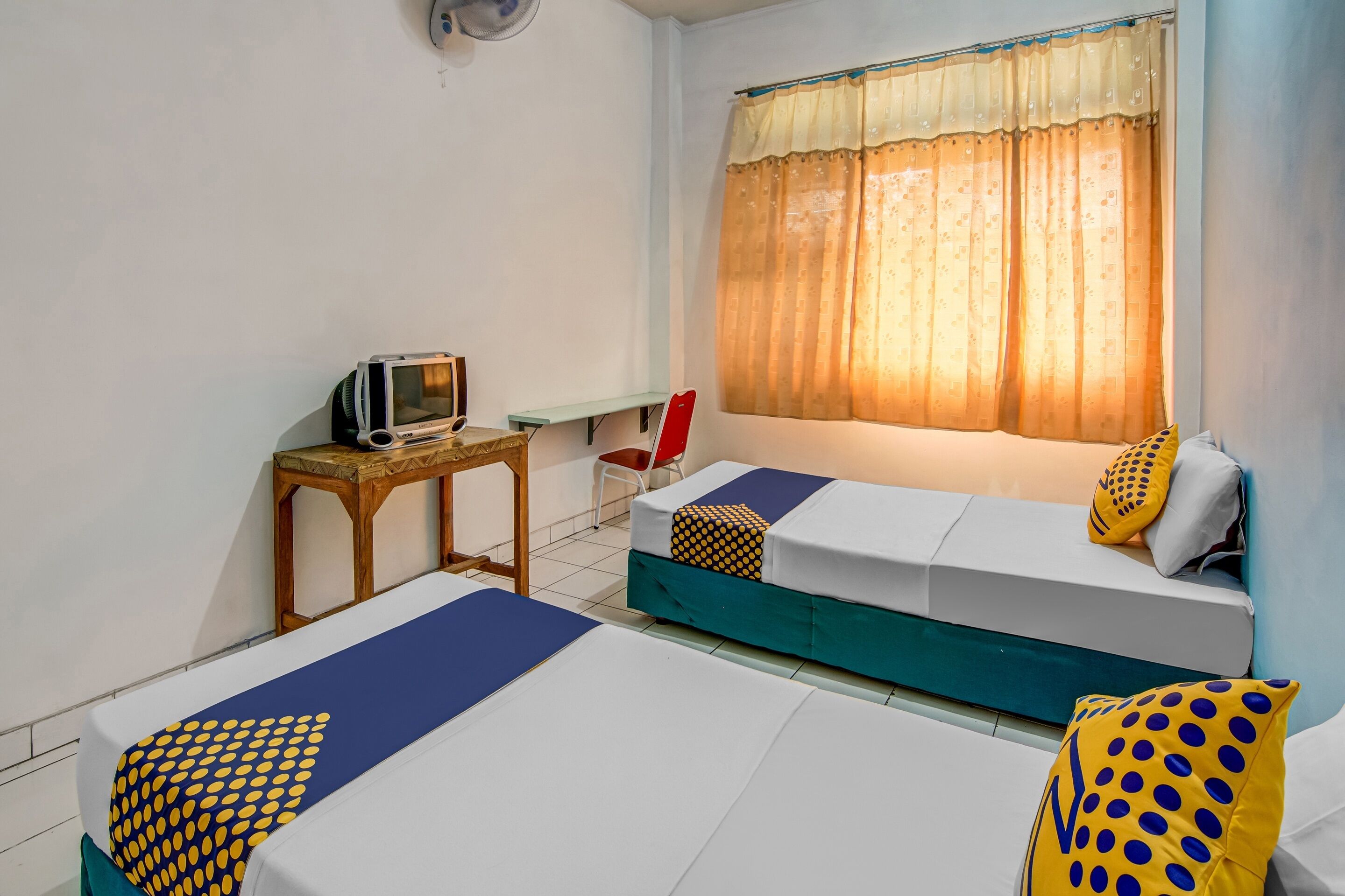 Une chambre avec deux lits, une petite table, une chaise, un téléviseur et une fenêtre avec des rideaux.