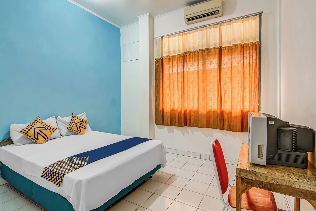 Una habitación de hotel con cama, escritorio con ordenador y ventana con cortinas.