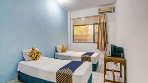A room with two beds, each with a white mattress and blue bedding, and a small wooden table with a green chair. - Spot ON 90964 Hotel Margadana (Tegal)