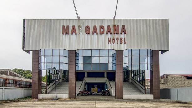 The exterior of the Matgadana Hotel with a prominent sign, a staircase leading to the entrance, and two motorcycles parked in front. - Spot ON 90964 Hotel Margadana (Tegal)
