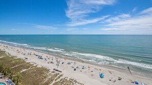 A beach with a clear sky, calm sea, and numerous umbrellas and people. - Bay Watch 1640-2BR Oceanfront - Corner Unit (North Myrtle Beach)
