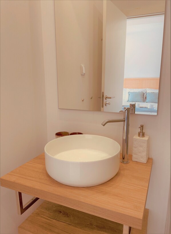 Une salle de bain avec un lavabo rond blanc, un miroir et un plan de toilette en bois.