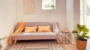 Un salon moderne avec un canapé gris, deux coussins jaunes, un tapis à motifs, une petite table ronde et une plante en pot.
