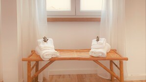 Une pièce avec un banc en bois placé sous une fenêtre, sur lequel reposent deux serviettes soigneusement pliées, ornées d’une feuille décorative.