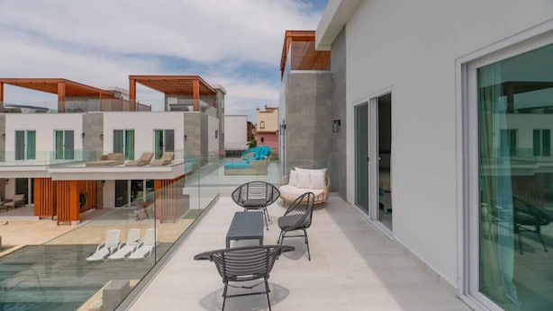 Un espace de vie extérieur moderne doté d’une piscine entourée de parois en verre, de chaises longues et d’un coin salon agrémenté de coussins.