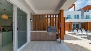 Un espace cuisine extérieur moderne, doté d’un comptoir intégré, d’un barbecue et d’un coin salon avec des fauteuils confortables.