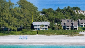 A beachfront property with a large house, a pool, and a beach with umbrellas. - Beach Condo with Quiet, Private Beach (Longboat Key)