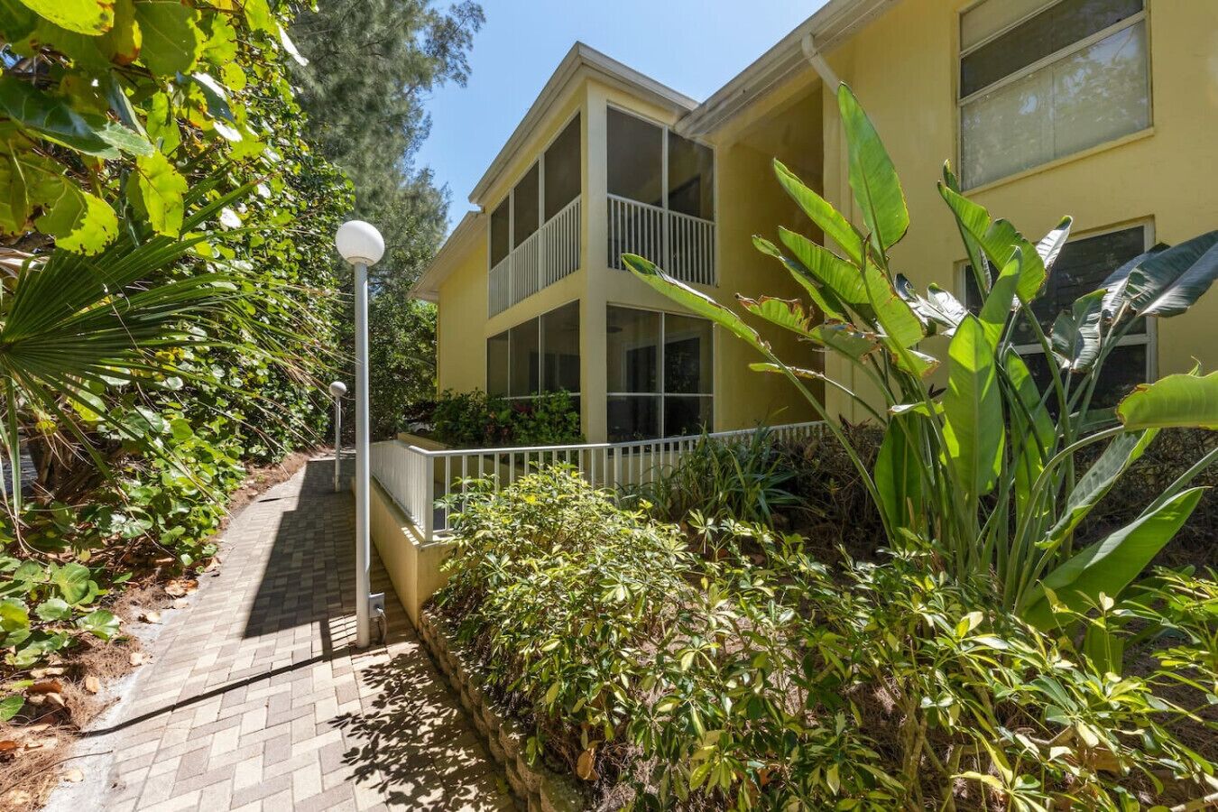 A two-story building with a balcony, surrounded by lush greenery and a paved walkway.