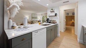 A modern kitchen with grey cabinets, a white countertop, and a dishwasher. There is a dining area with a sofa and a coffee machine. - Beach Condo with Quiet, Private Beach (Longboat Key)