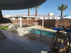 A pool area with a fenced deck, lounge chairs, and a hanging chair.