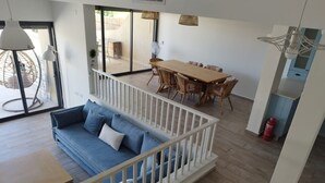 A modern living room with a blue sofa, a wooden dining table with wicker chairs, and a white railing. - YalaRent Cliff side villa - private pool (Eilat)