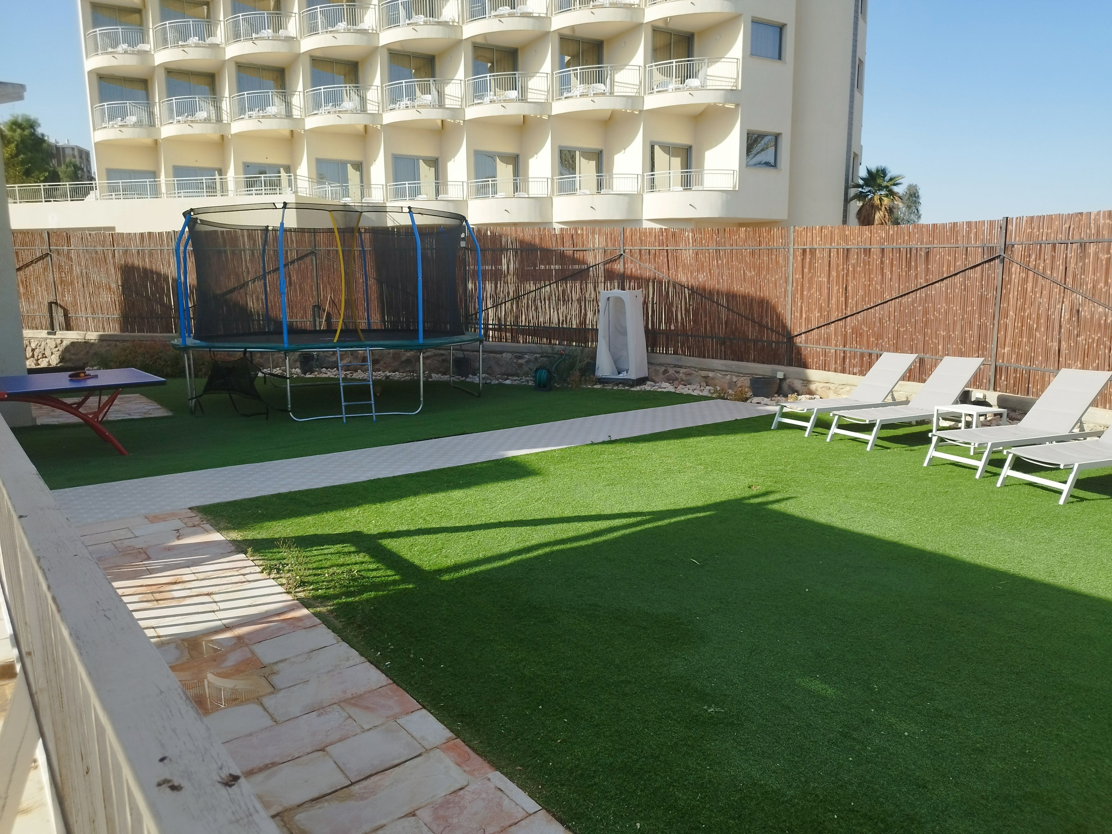 Ein Garten mit Kunstrasen, einem Trampolin, Liegestühlen und einem Billardtisch.