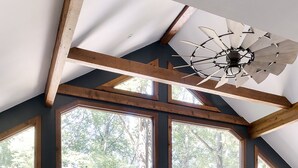 Un salón amplio con ventanas grandes, vigas de madera y un ventilador de techo.