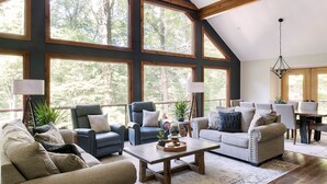 Un salón espacioso con ventanas amplias, un techo alto con vigas a la vista y un comedor con mesa y sillas de madera.