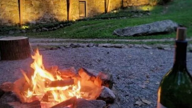 Una casa moderna con fachada de piedra y ventanas amplias, un brasero al frente y una botella de vino.