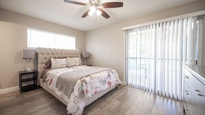 Ein Schlafzimmer mit Bett, Deckenventilator, Nachttisch, Kommode und einem Fenster mit Jalousien.