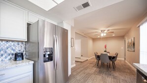 Eine moderne Küche mit Edelstahlgeräten, ein Essbereich mit Tisch und Stühlen sowie ein Deckenventilator.