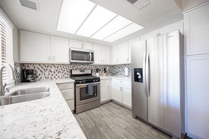 A modern kitchen with white cabinets, a stainless steel refrigerator, a microwave, and a gas stove.