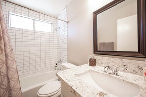Ein Badezimmer mit Badewanne, Toilette und Waschbecken mit großem Spiegel.