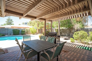 An outdoor patio with a pool, a grill, and a table with chairs.