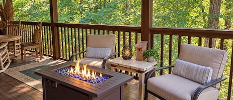 A covered outdoor deck with a fire feature, seating, and a view of a forest.