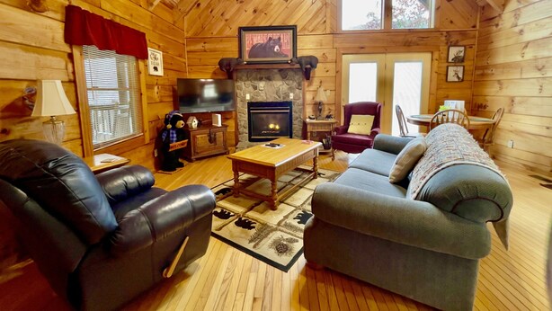 A cozy log cabin interior with a fireplace, leather sofas, a television, and a stone wall.