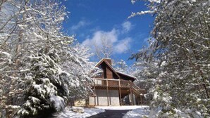 A wooden cabin with a balcony, surrounded by snow-covered trees.
