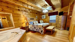 A log cabin bedroom with a large bed, a wooden dresser, a vanity, and a ceiling fan.