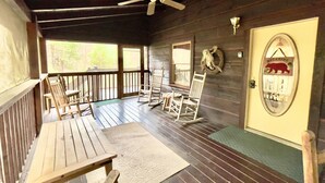 A wooden porch with a ceiling fan, a welcome sign, and a door with a bear decoration.