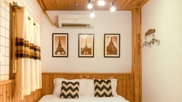 A bedroom with a wooden headboard, a bed with white bedding, three framed pictures of the Eiffel Tower, and a wall-mounted air conditioner. - WuzhenThose Years, Those Events, Those People (Tongxiang)