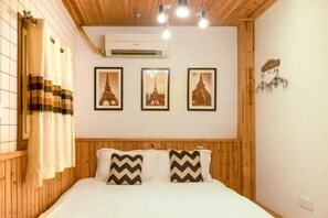 A bedroom with a wooden headboard, a bed with white bedding, three framed pictures of the Eiffel Tower, and a wall-mounted air conditioner. - WuzhenThose Years, Those Events, Those People (Tongxiang)