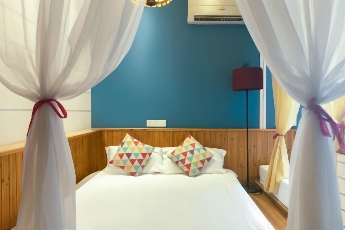 A bedroom with a bed, white curtains tied with red ribbons, a blue wall, and a wooden headboard.
