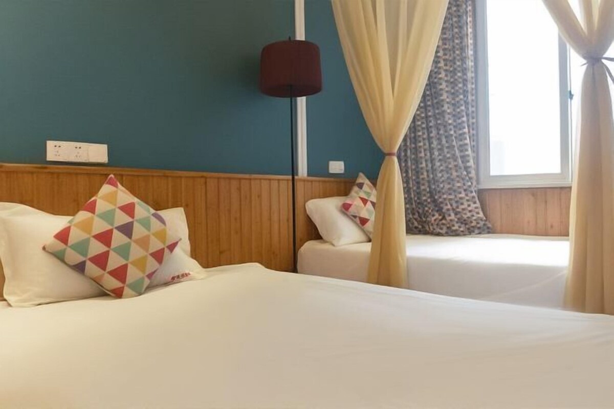 A hotel room with two beds, a wooden headboard, a lamp, and a window with curtains.