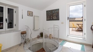 Una habitación con una escalera de caracol, una ventana con vistas a un patio, y un cuadro en la pared.