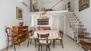 Un comedor con una mesa dispuesta para cuatro personas, rodeada de sillas de madera. Se ve una estantería de madera y un radiador al fondo.
